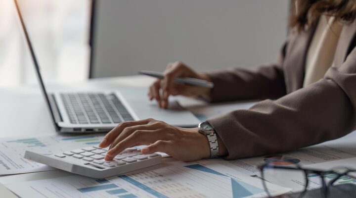 Person mit Taschenrechner und Laptop beim Auswerten von Finanzunterlagen