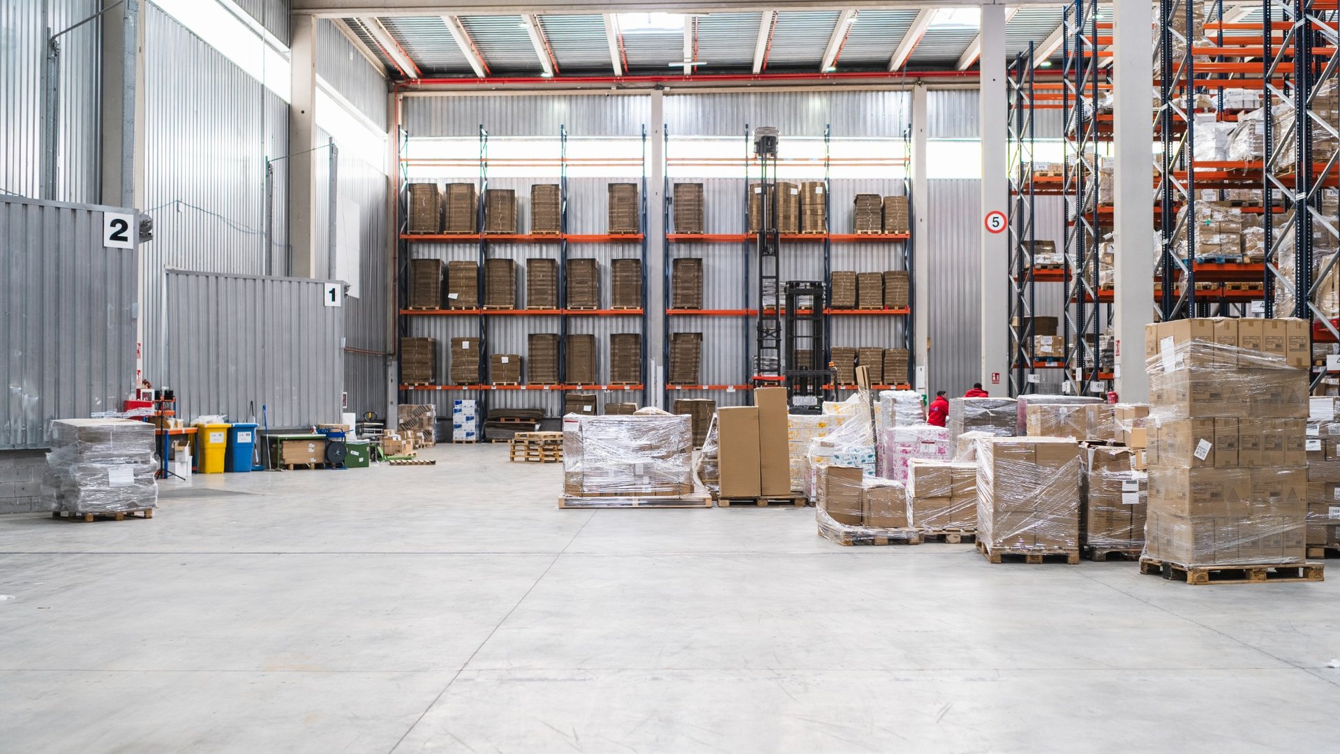 - Innenansicht einer großen Lagerhalle mit Regalen, Paletten und verpackten Waren.